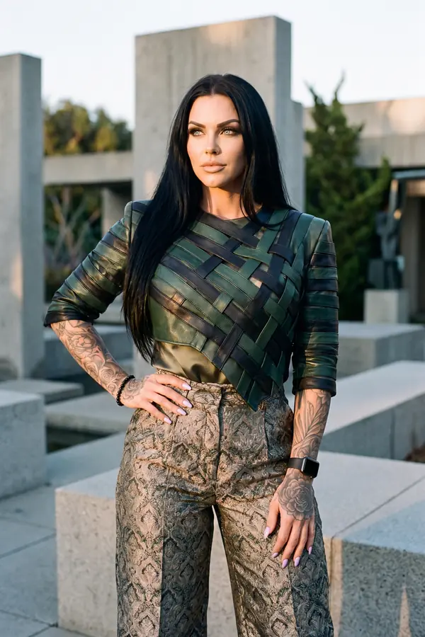 Woman in a green and black woven leather top with bronze brocade wide-leg trousers among granite blocks at sunset